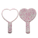 Pink rhinestone heart-shaped Suumee handheld mirror displayed on marble vanity surface