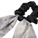 Model smiling while adjusting black bow hair tie in natural daylight