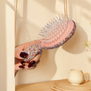 Cushion hairbrush in use on shoulder-length wavy hair — lifestyle styling shot