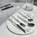 Pearl-embellished stainless steel cutlery set laid out on white marble surface